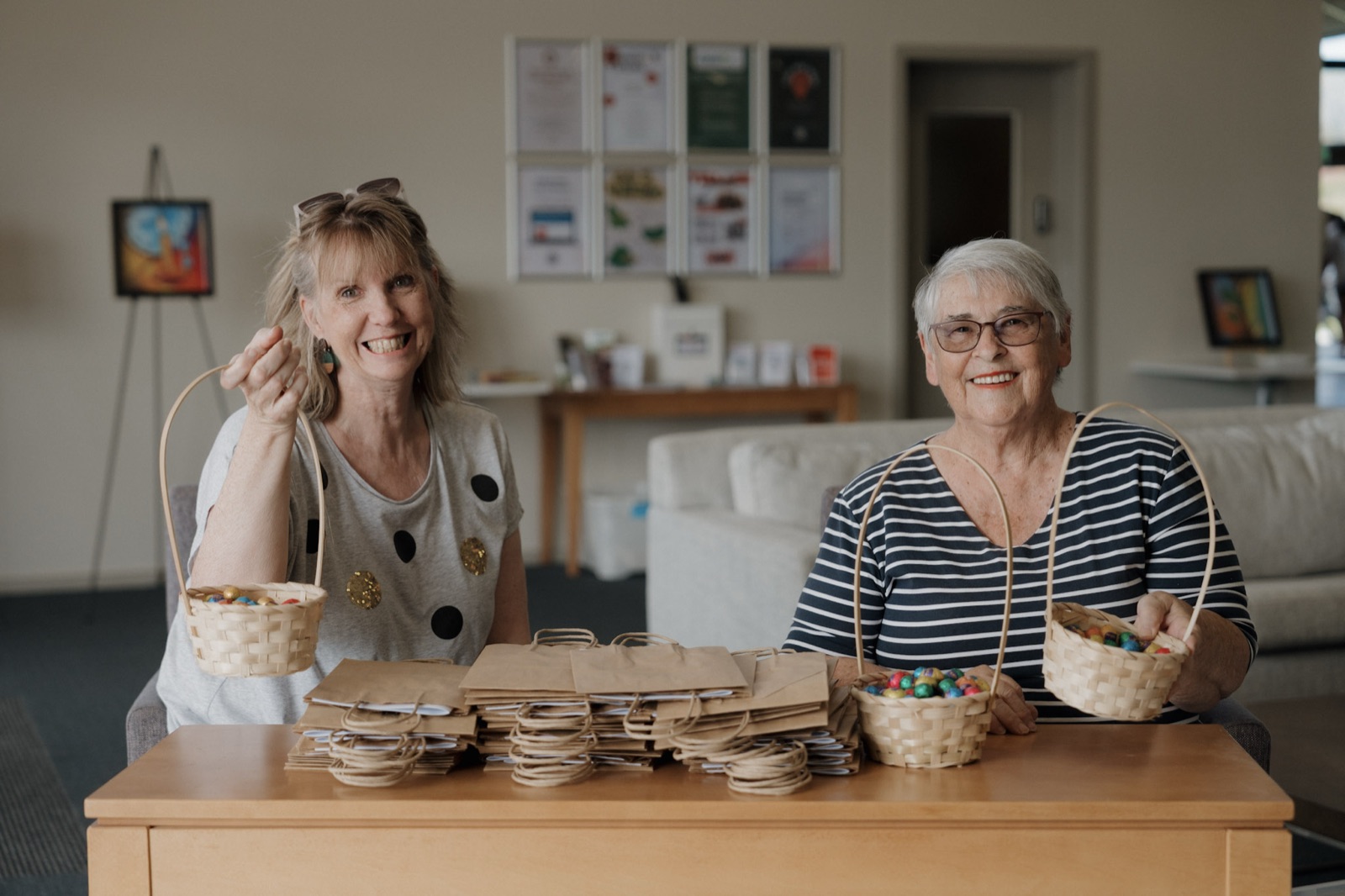 Two women of Village Baptist at a table in the church foyer, holding up baskets